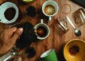 Hand pouring coffee into various cups with spills on wooden table.