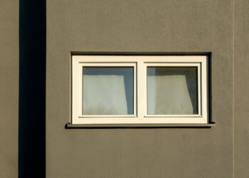 A minimalist white window on a textured concrete wall casting shadows in sunlight.
