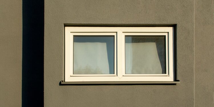 A minimalist white window on a textured concrete wall casting shadows in sunlight.