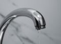 A close-up shot of a modern chrome bathroom faucet with water dripping from the tip.