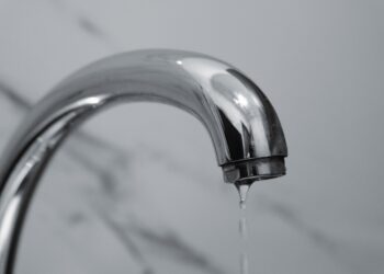 A close-up shot of a modern chrome bathroom faucet with water dripping from the tip.