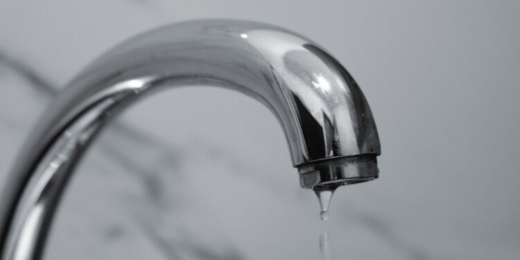 A close-up shot of a modern chrome bathroom faucet with water dripping from the tip.