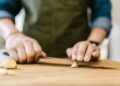 Close-up of a person slicing garlic on a wooden cutting board, emphasizing cooking preparation.