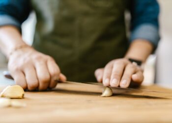 Close-up of a person slicing garlic on a wooden cutting board, emphasizing cooking preparation.