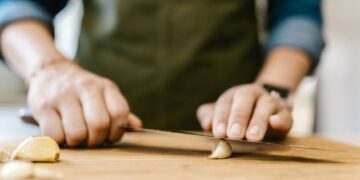 Close-up of a person slicing garlic on a wooden cutting board, emphasizing cooking preparation.