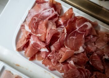 Freshly sliced prosciutto ham served on a white tray in the kitchen.
