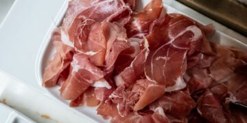Freshly sliced prosciutto ham served on a white tray in the kitchen.