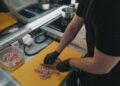 Man slicing raw meat on a yellow cutting board in a modern kitchen setting.