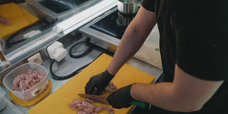 Man slicing raw meat on a yellow cutting board in a modern kitchen setting.
