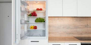 Contemporary kitchen with refrigerator filled with fresh bright tomatoes lettuce and bell peppers