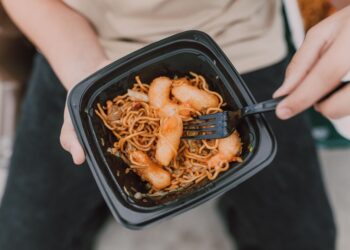 Tasty Asian noodles with shrimp in a black container held by a person.