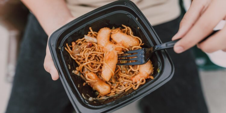 Tasty Asian noodles with shrimp in a black container held by a person.