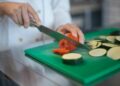Chef precisely slices tomato and zucchini on green board, enhancing culinary presentation.