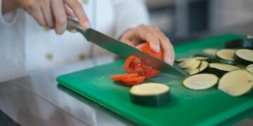 Chef precisely slices tomato and zucchini on green board, enhancing culinary presentation.