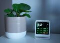Air quality monitor next to a potted plant on a desk, showing CO2 and PM2.5 levels.