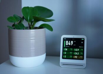 Air quality monitor next to a potted plant on a desk, showing CO2 and PM2.5 levels.