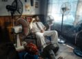 Man in white suit relaxing amongst multiple fans in a retro-themed room.