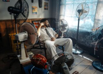Man in white suit relaxing amongst multiple fans in a retro-themed room.