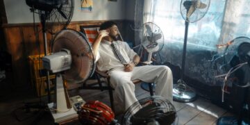Man in white suit relaxing amongst multiple fans in a retro-themed room.