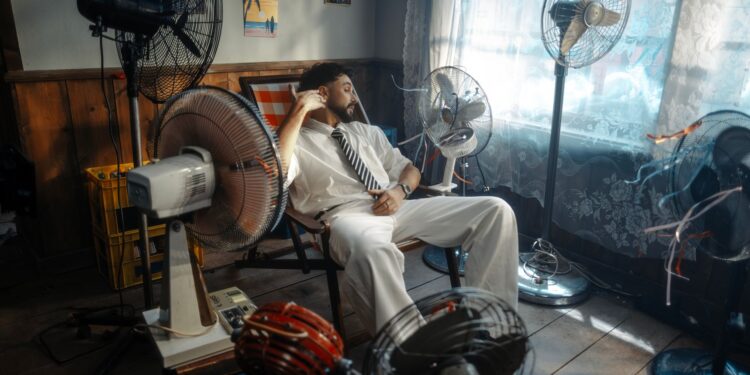 Man in white suit relaxing amongst multiple fans in a retro-themed room.