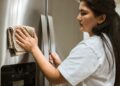 A woman wipes a refrigerator with a cloth, focusing on maintaining cleanliness in a kitchen.
