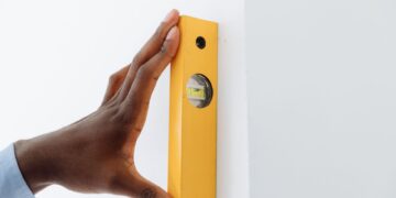 A close-up of a hand using a yellow level tool against a white wall to ensure vertical alignment.