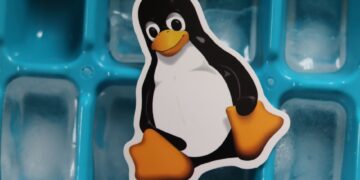 Close-up of a Linux penguin sticker placed on a blue ice cube tray with frozen cubes.