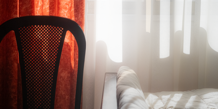 Sunlight streaming through curtains illuminating a bed and chair in a cozy bedroom setting.