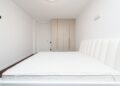 Contemporary minimalist bedroom featuring a white mattress and sleek wardrobe under soft lighting.