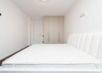 Contemporary minimalist bedroom featuring a white mattress and sleek wardrobe under soft lighting.