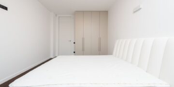 Contemporary minimalist bedroom featuring a white mattress and sleek wardrobe under soft lighting.