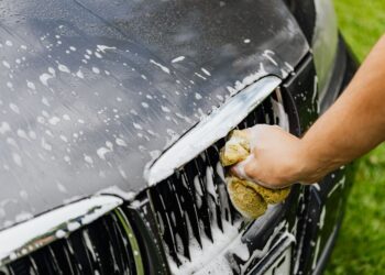 Detailed view of a hand washing a car grille with a soapy sponge outdoors.