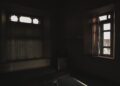 Dark room with open windows casting soft light and shadows creating a moody atmosphere.