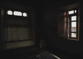 Dark room with open windows casting soft light and shadows creating a moody atmosphere.