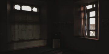 Dark room with open windows casting soft light and shadows creating a moody atmosphere.