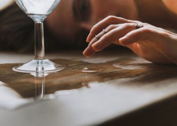A close-up shot of a hand touching a water droplet next to a glass on a wooden surface.