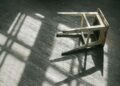 A worn wooden stool casting shadows on a sunlit wooden floor, creating a rustic and moody ambiance.