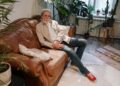 Elderly man relaxing on a leather sofa in a cozy indoor setting with plants.