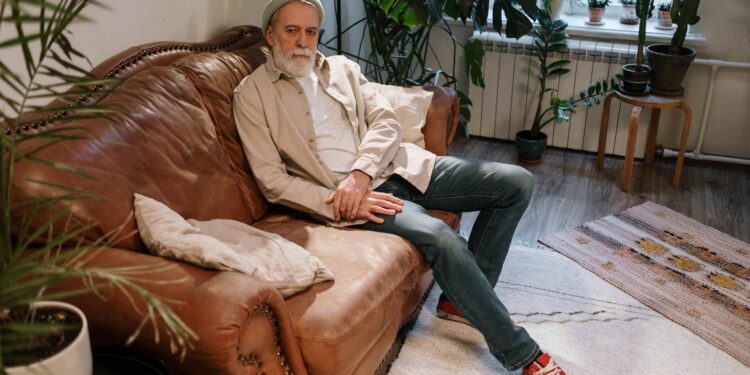 Elderly man relaxing on a leather sofa in a cozy indoor setting with plants.
