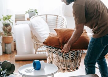 A man packing up a basket with cushions and blankets in a bright, cozy living room.