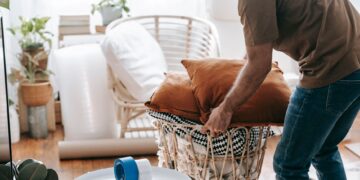 A man packing up a basket with cushions and blankets in a bright, cozy living room.
