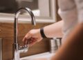 Close-up of a person's hand turning a chrome faucet handle in a modern bathroom setting.