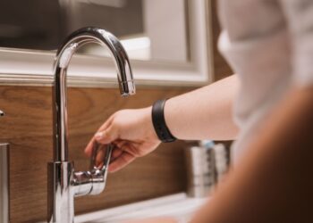 Close-up of a person's hand turning a chrome faucet handle in a modern bathroom setting.