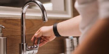 Close-up of a person's hand turning a chrome faucet handle in a modern bathroom setting.