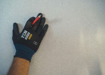 A gloved hand holding a pencil against a textured wall surface, ready for repair work.