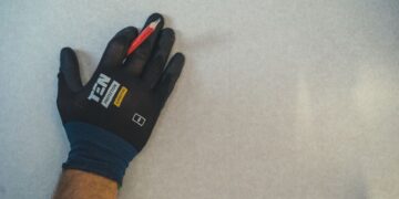 A gloved hand holding a pencil against a textured wall surface, ready for repair work.