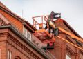 Roofer in a cherry picker conducting maintenance on a red brick building with a tiled roof.