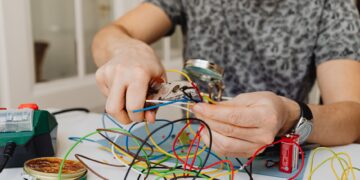 Person using pliers to cut through colorful electrical wires, showcasing DIY electronics work.