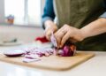 Close-up of a woman chopping fresh red onion in a kitchen setting.