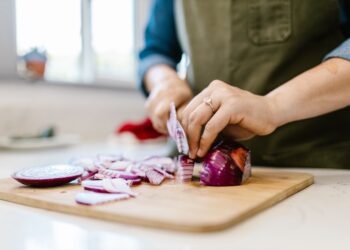 Close-up of a woman chopping fresh red onion in a kitchen setting.